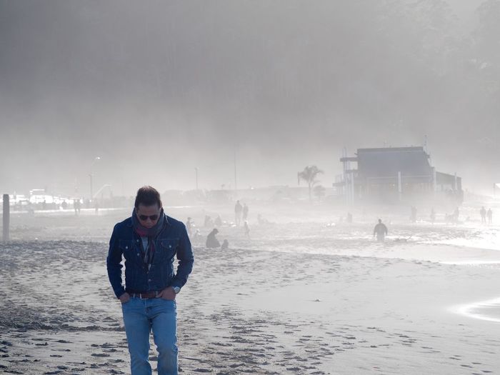 Man walking at beach against sky during foggy weather