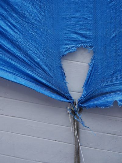 Torn blue tarpaulin on white wall