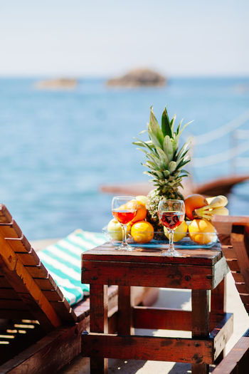 Close-up of drink and fruits on table by lounge chair against sea