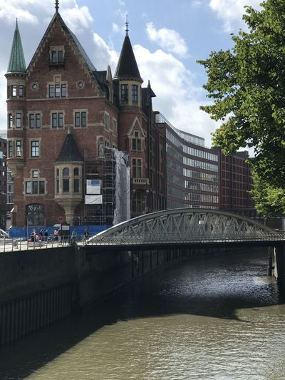 Bridge over river by buildings in town against sky