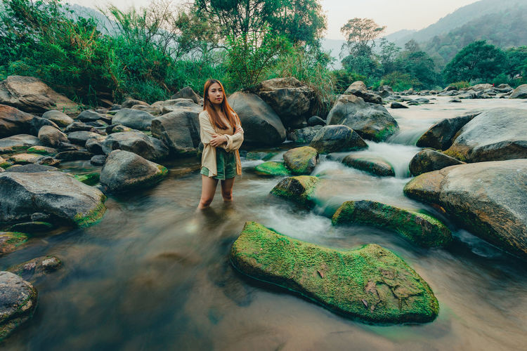 Young woman standing on rock by stream