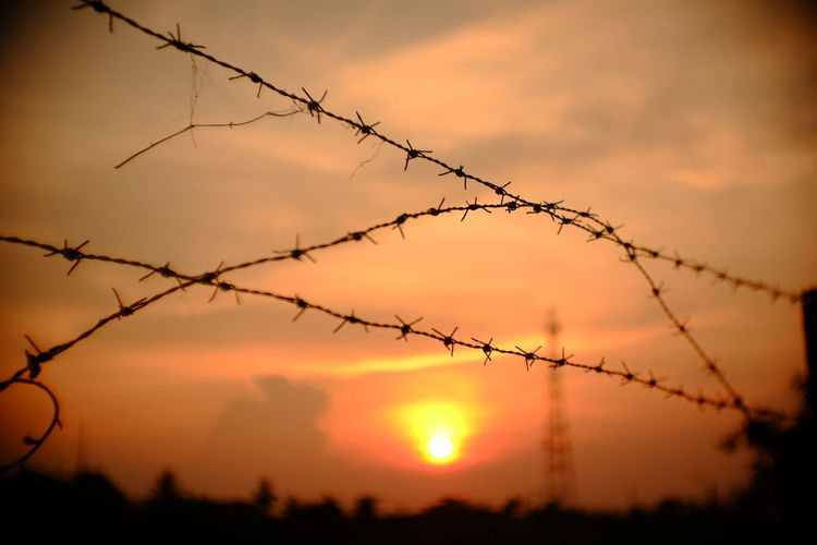 Silhouette barbed wire against sky during sunset