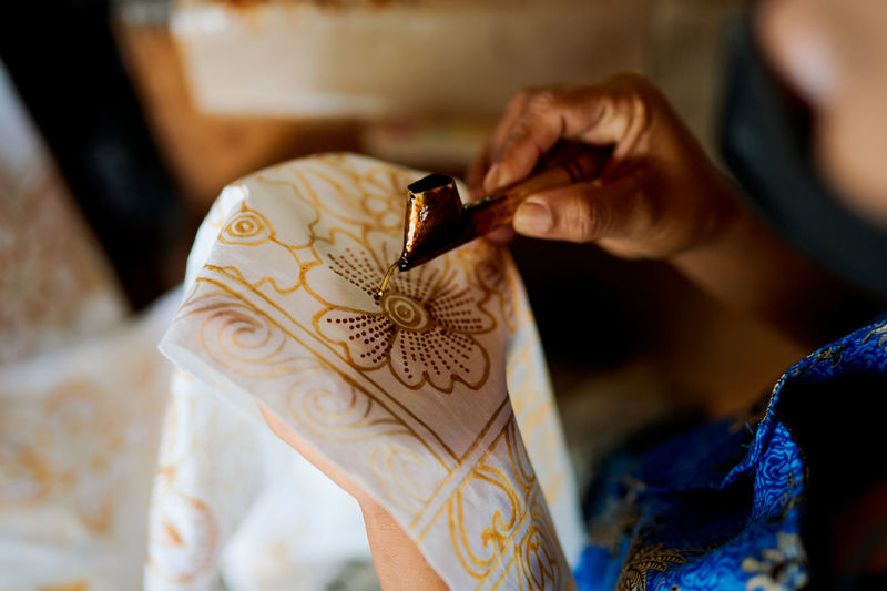 Close up of woman painting batik on a white cloth with wax