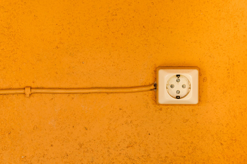 Close-up of electric outlet on orange wall
