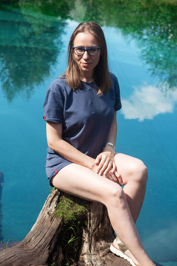 Portrait of woman sitting on tree stump by lake