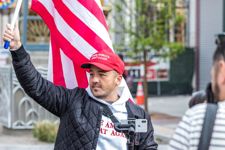 Man with flag and maga hat standing in city