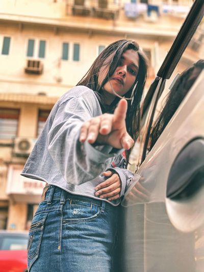 Portrait of woman gesturing standing by car in city