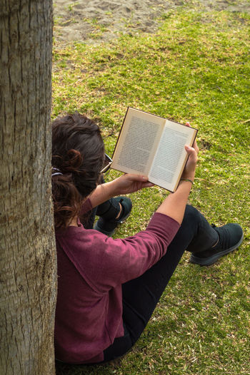 Midsection of woman reading book by tree trunk