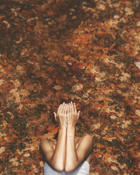 Directly above view of woman lying on fallen dry leaves while covering face