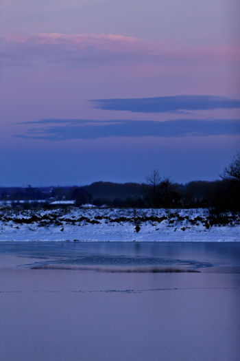 Scenic view of frozen land against sky at sunset
