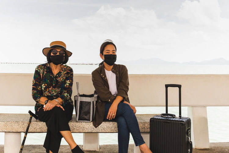 Full length of femals wearing protective mask and sunglasses sitting against sky