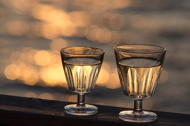 Close-up of drinks on railing against sea during sunset