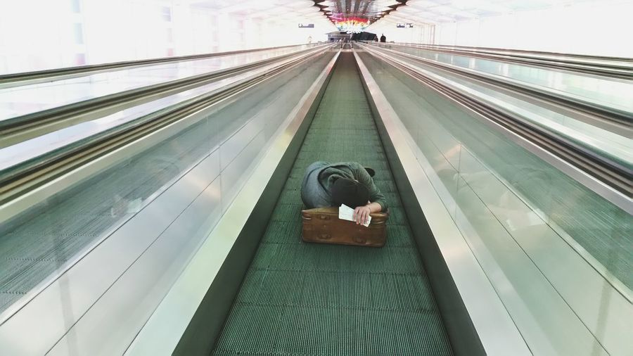 Man sleeping on suitcase on moving walkway