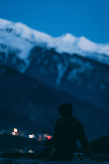 Rear view of silhouette woman sitting against snow covered mountain at dusk