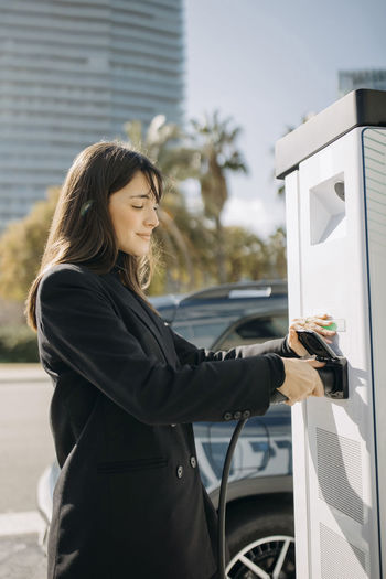 Smiling woman charging electric car at charging station