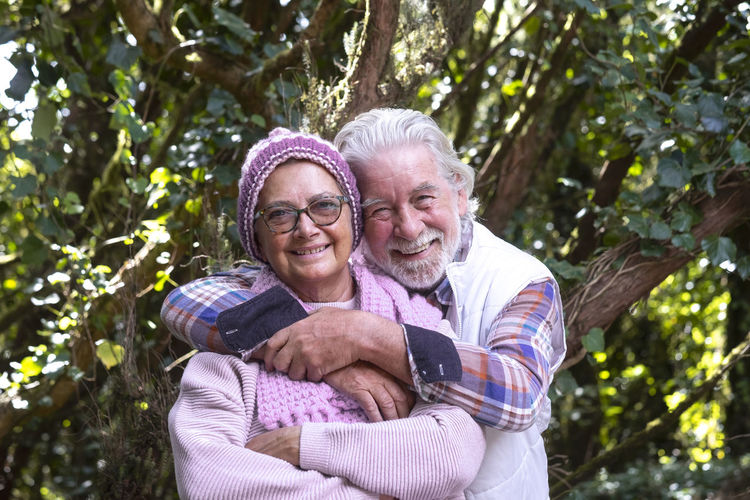 Portrait of smiling senior couple sitting by tree outdoors