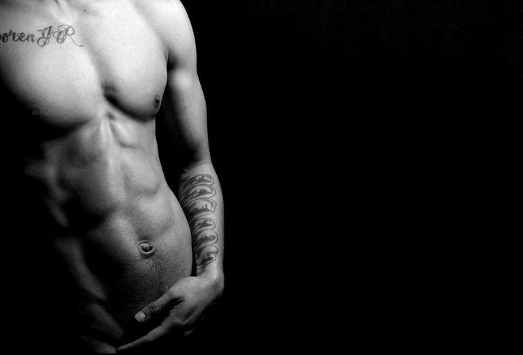 Midsection of shirtless muscular man against black background