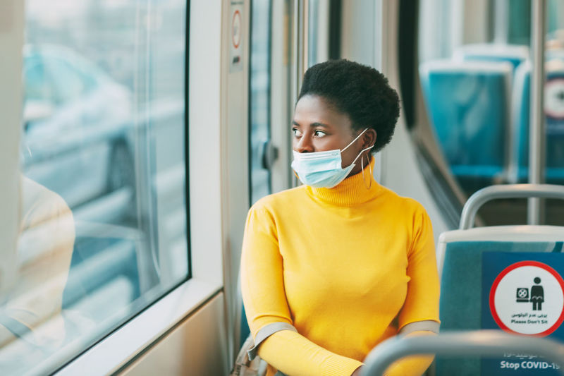 Dubai, uae, november 2020 a young african woman wearing a protective mask rides on a bus and looks