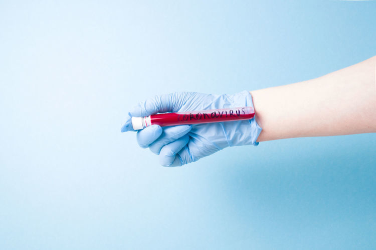 Close-up of woman hand holding test tube against blue background