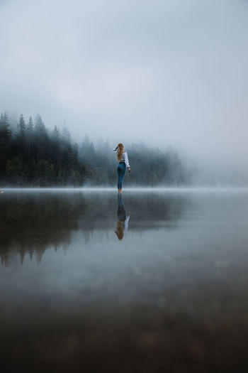 Young caucasian blonde woman standing in the calm forest foggy lake.	