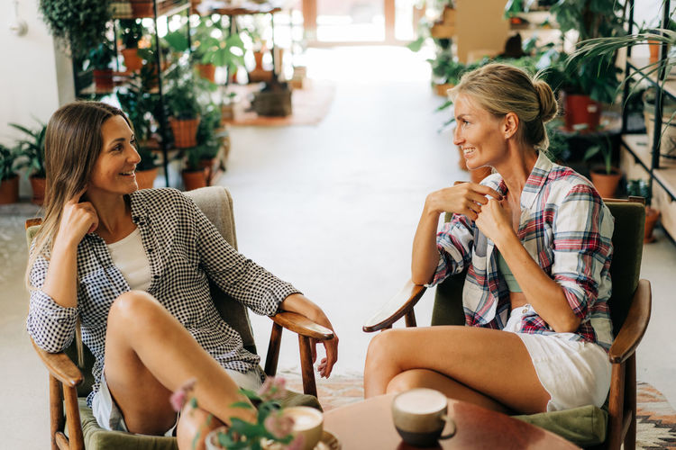Two young attractive women are chatting cheerfully while sitting in a cozy cafe.