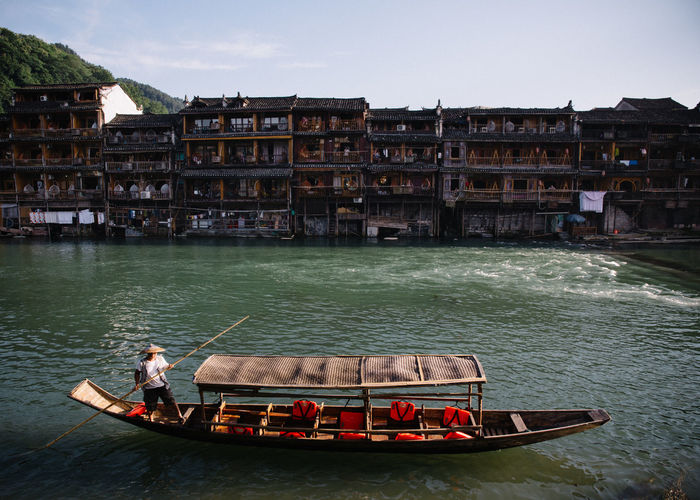 Man on gondola in canal against buildings during sunny day