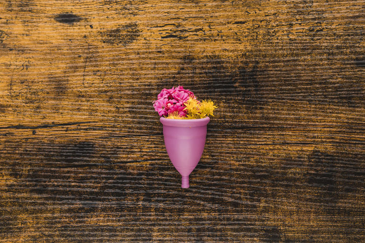 Menstrual cup with flowers on wooden background