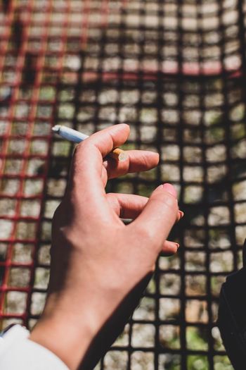 Close-up of cropped hand holding cigarette by metal grate