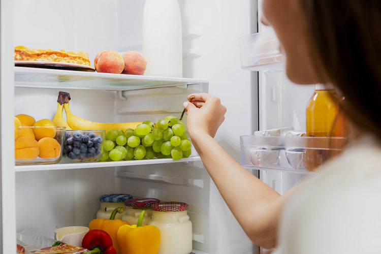 Woman hand taking, grabbing or picks up green bunch of grapes out of open refrigerator or fridge