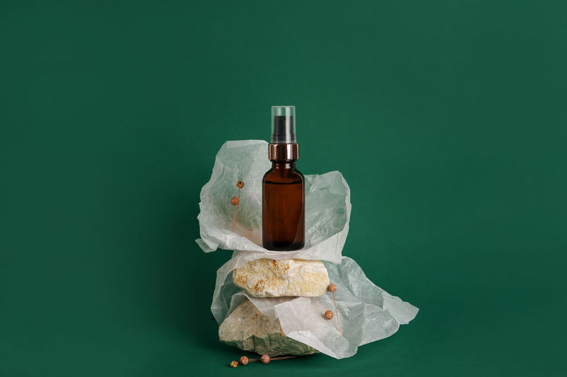 Glass bottle of moisturizing face serum, cosmetic oil on stones on green background