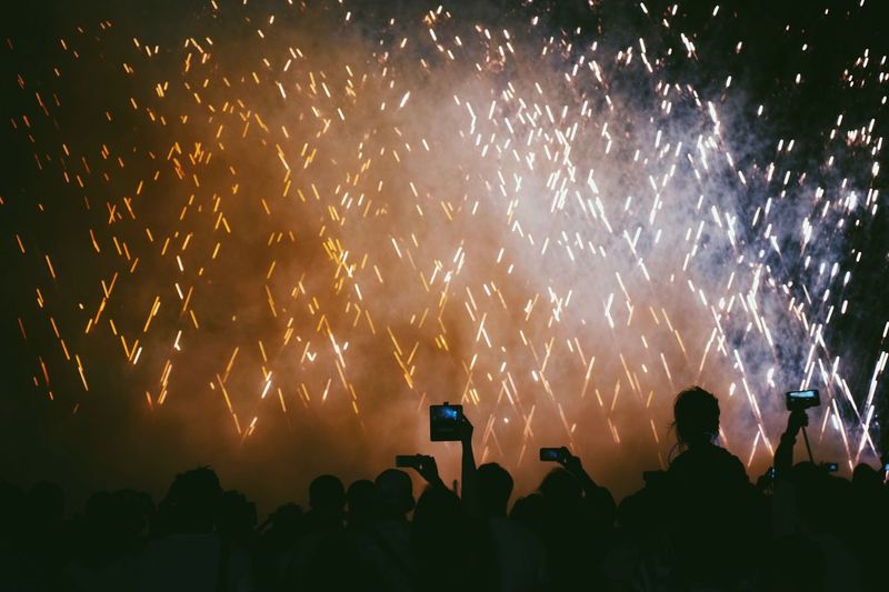 Low angle view of silhouette people photographing firework display at night