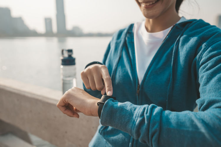 Midsection of woman touching smart watch while standing outdoors