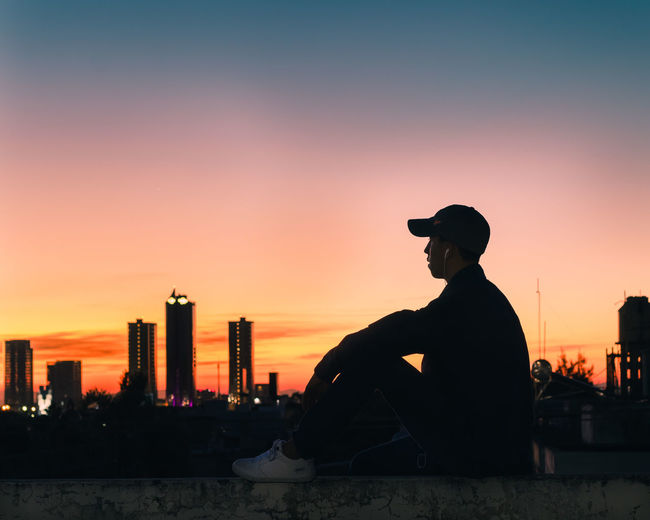 Silhouette man sitting against orange sky
