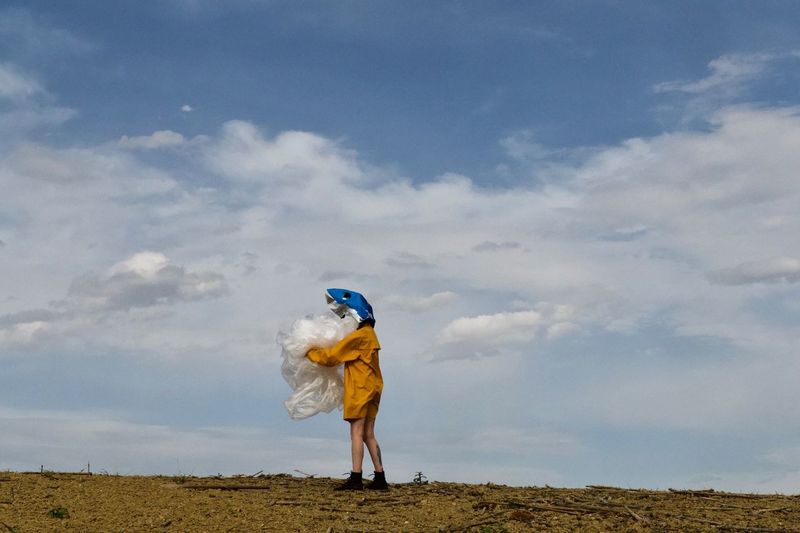 Woman wearing mask holding fabric against sky on land