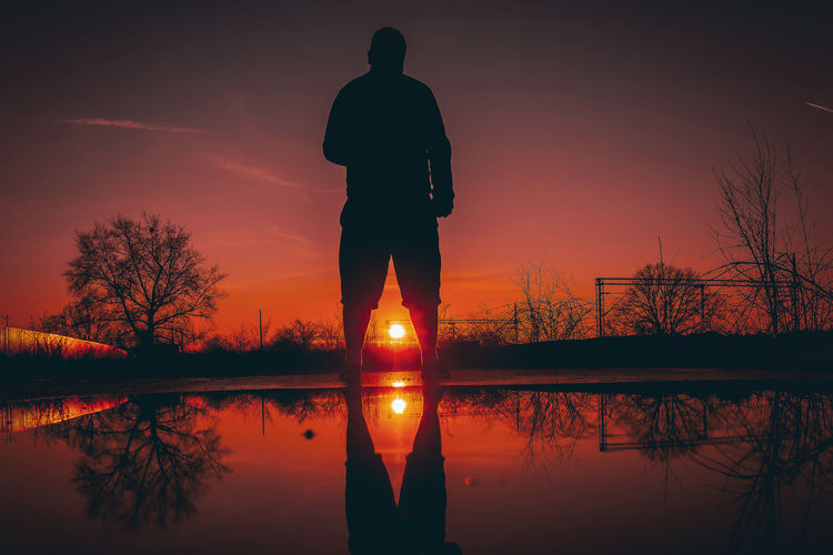 Silhouette man standing by lake against sky during sunset