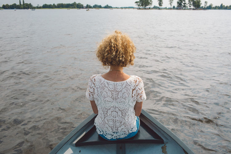 Rear view of mid adult woman sitting in boat on lake