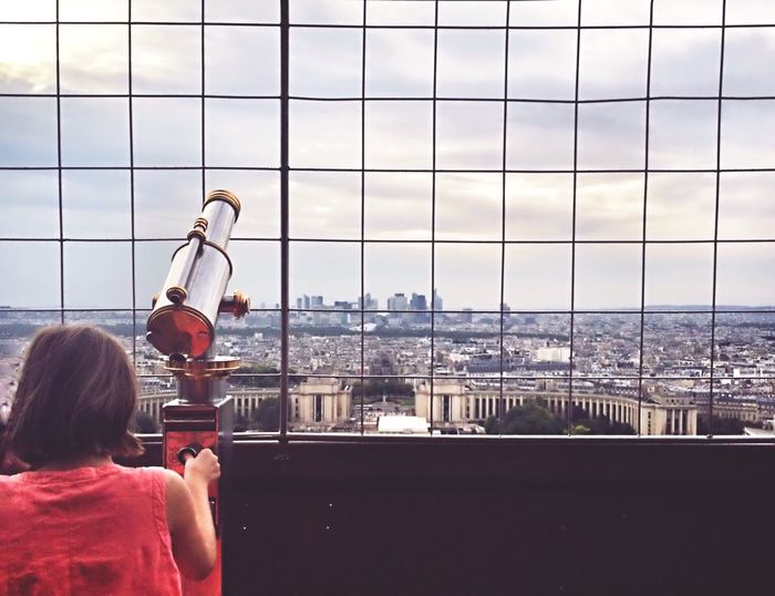 Rear view of girl using coin operated binoculars against cityscape