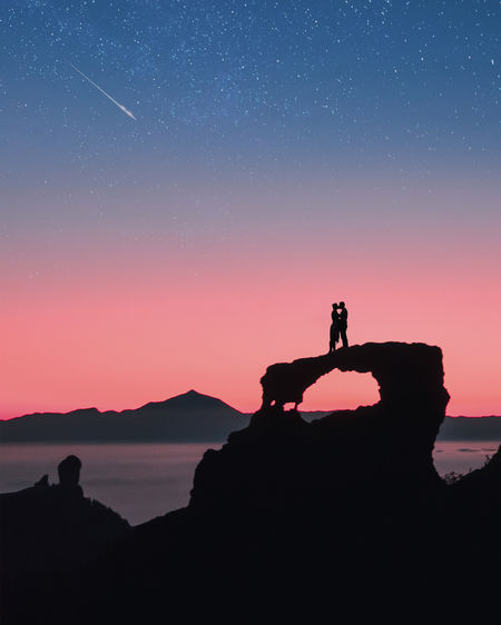 Silhouette man standing on mountain against sky at night