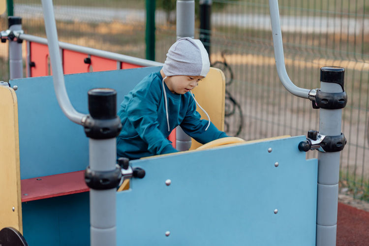 Cute little boy with down syndrome in a funny hat walks in the playground