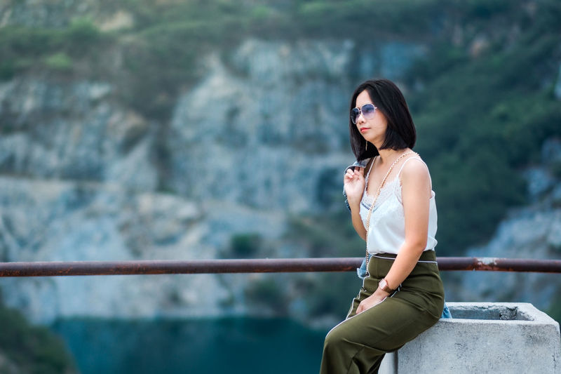 Beautiful woman looking away while sitting against cliff