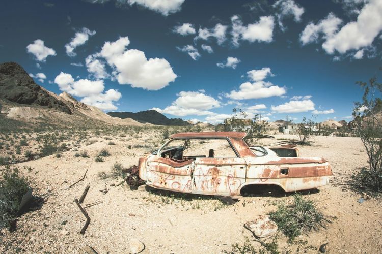 Old damaged car on arid landscape against cloudy sky during sunny day
