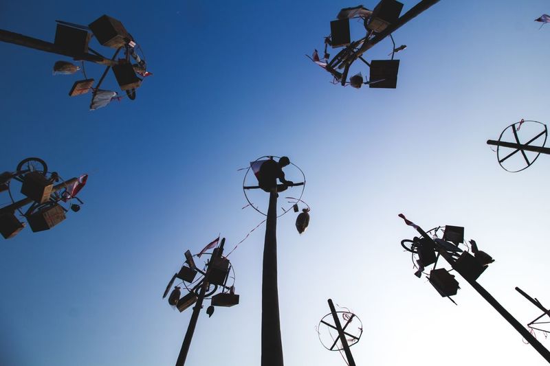 Low angle view of silhouette man hanging objects on pole against clear sky