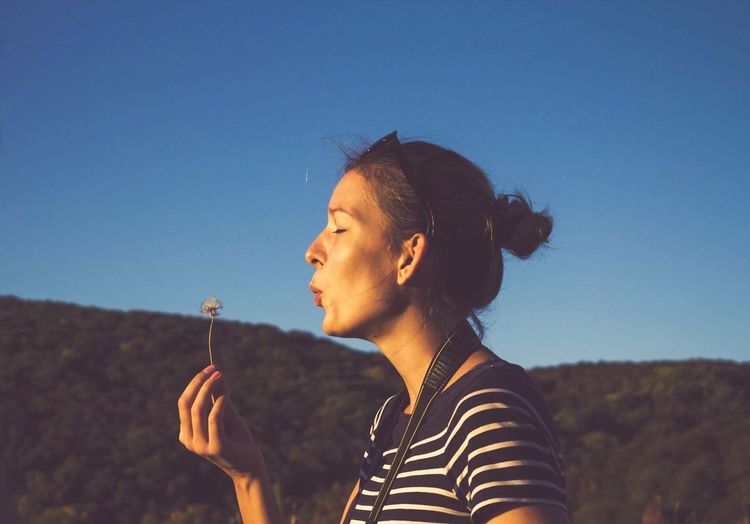 Young woman blowing dandelion against clear blue sky