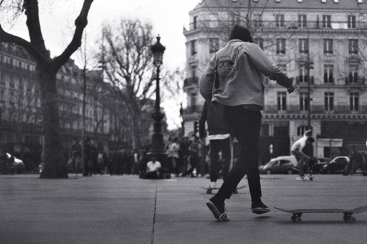 Rear view of man by skateboard on footpath against buildings