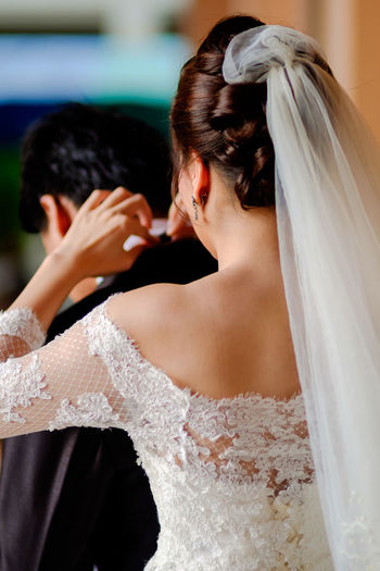 Rear view of bride helping bridegroom to get dressed