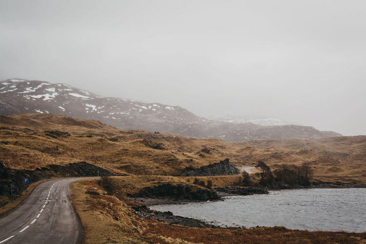 Country road leading towards mountains against sky during winter