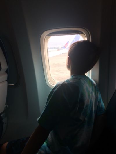 Rear view of boy looking out of airplane window