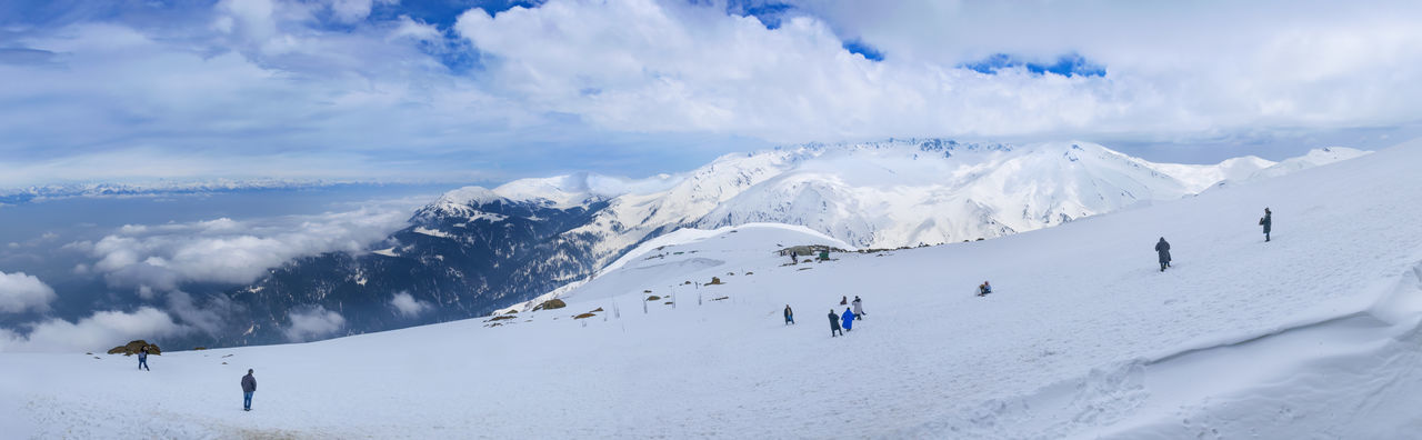 Panoramic view of people skiing on snowcapped mountain against sky