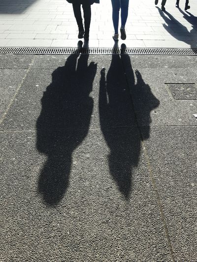Low section of people with shadow walking on footpath during sunny day