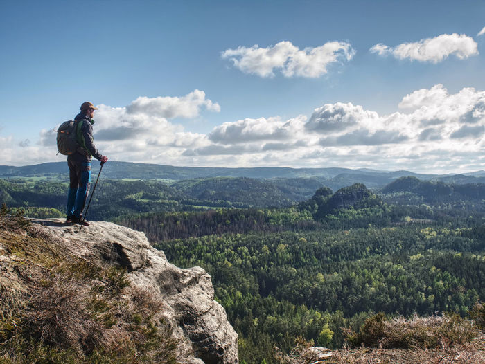 Tourist on trail, walk on sandstone hill, wearing backpack and sunglasses, using trekking sticks